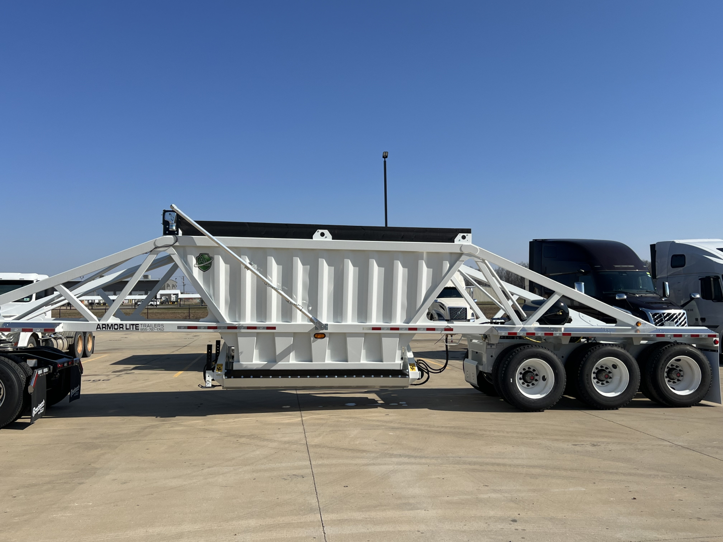 Armor Lite SBD42 tri-axle dump trailer with air ride and skeleton frame, white and silver, attached to a trailer truck in a dealership lot.