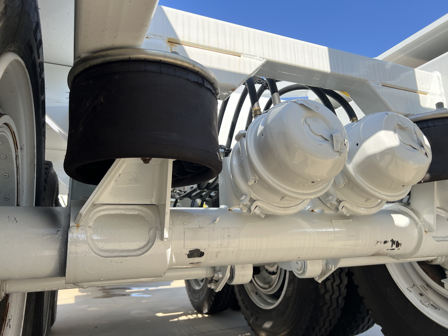 Trailer suspension system with air ride components and axles visible under a white Armor Lite SBD42 tri-axle. Close-up view shows air bags, hoses, and metallic frame.