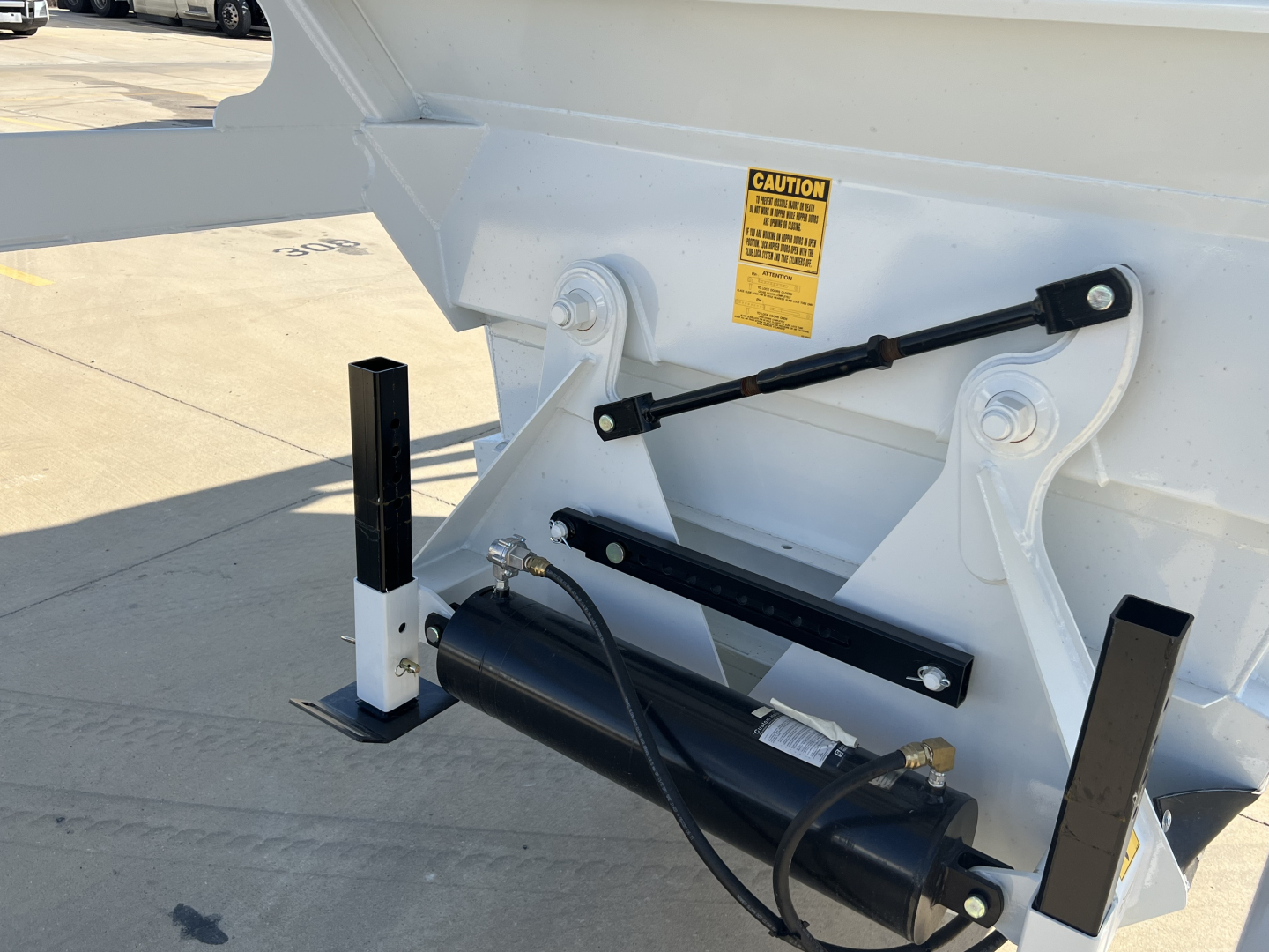 Dump trailer tail section with hydraulic air ride system housing and warning label showing hydraulic actuator and support brackets.