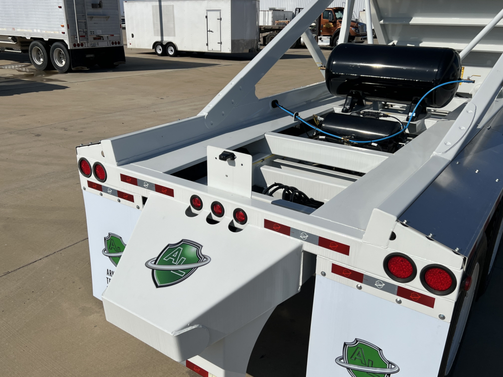 Dump trailer rear view showing white Armor Lite SBD42 tri-axle air ride suspension, rear lights, and green emblem patches on each mud flap.