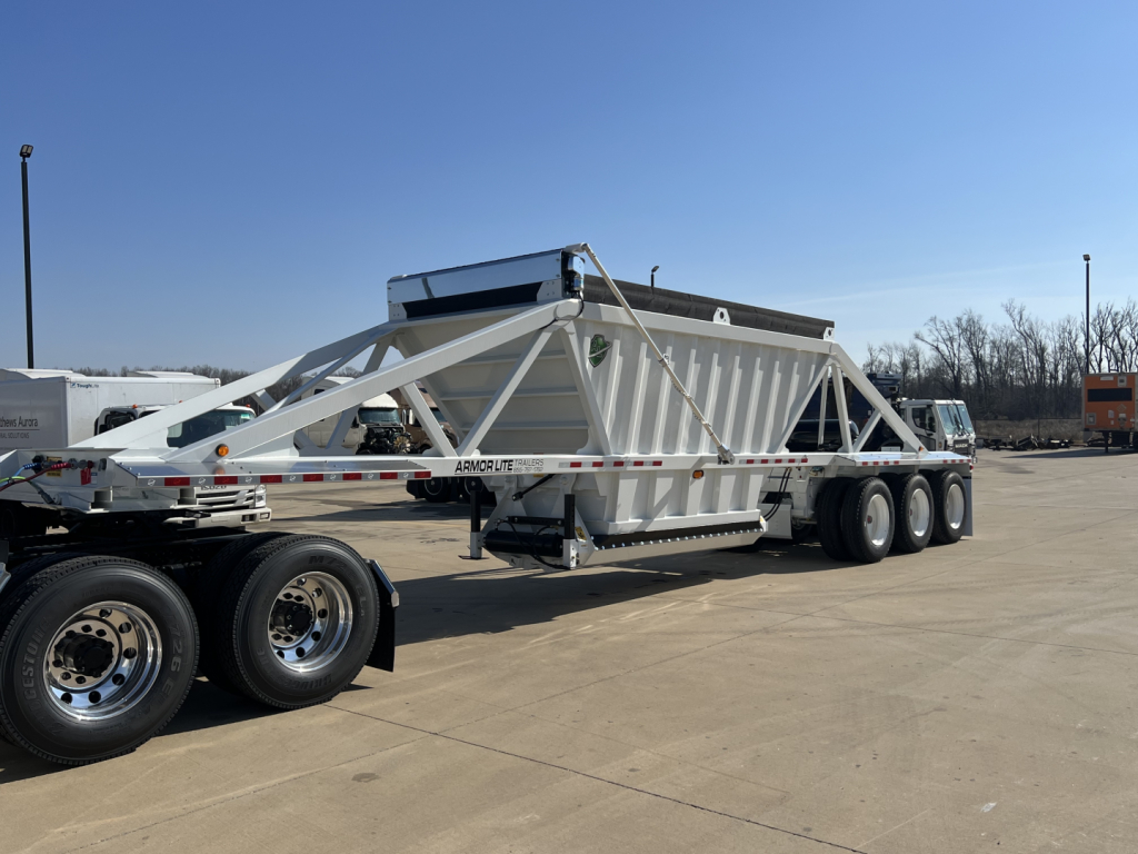 aluminum tri-axle dump trailer with air ride suspension and skeleton frame, attached to a semi truck in a dealership lot, Armor Lite SBD42 model label not visible