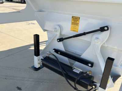 Dump trailer tail section with hydraulic air ride system housing and warning label showing hydraulic actuator and support brackets.