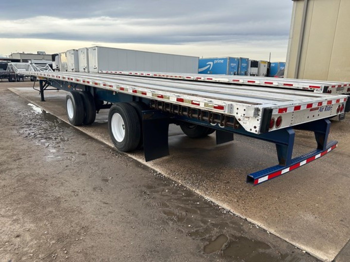 Flatbed trailer showing dual rear axles and long aluminum deck with side rails and reflective tape, Great Dane Freedom LT trailer in outdoor lot.