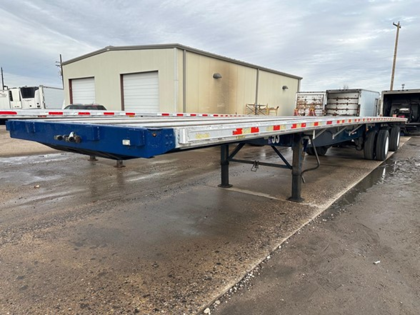 Flatbed trailer showing metal deck and tandem axle with blue frame and support legs.