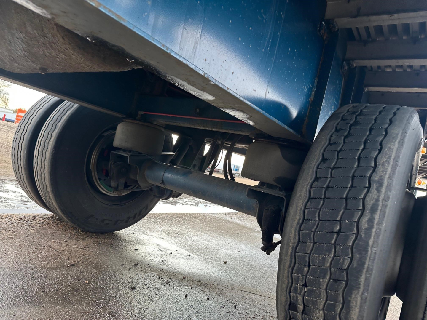 Rear undercarriage of a flatbed trailer showing dual rear wheels, suspension components, and undercarriage frame.