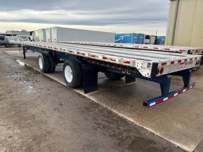 Flatbed trailer showing dual rear axles and long aluminum deck with side rails and reflective tape, Great Dane Freedom LT trailer in outdoor lot.