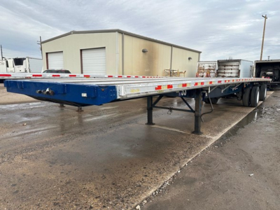 Flatbed trailer showing low-profile deck and dual rear axles with reflective tape along sides.