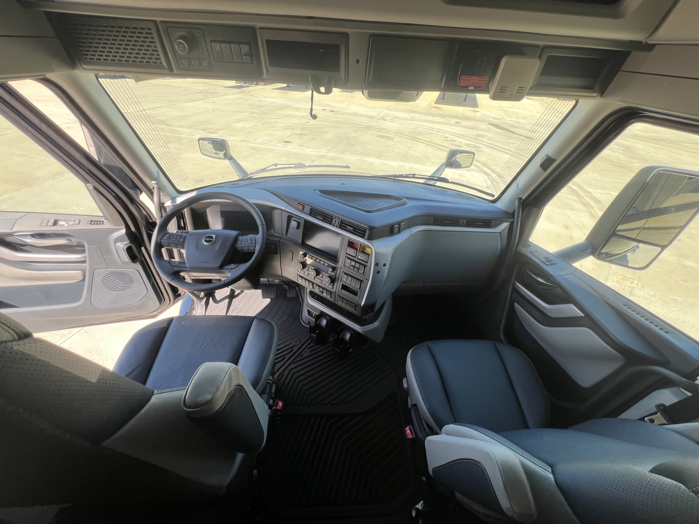 Cab interior of a Volvo VNL tractor showing steering wheel, dashboard, and two front seats with center console and large windshield.