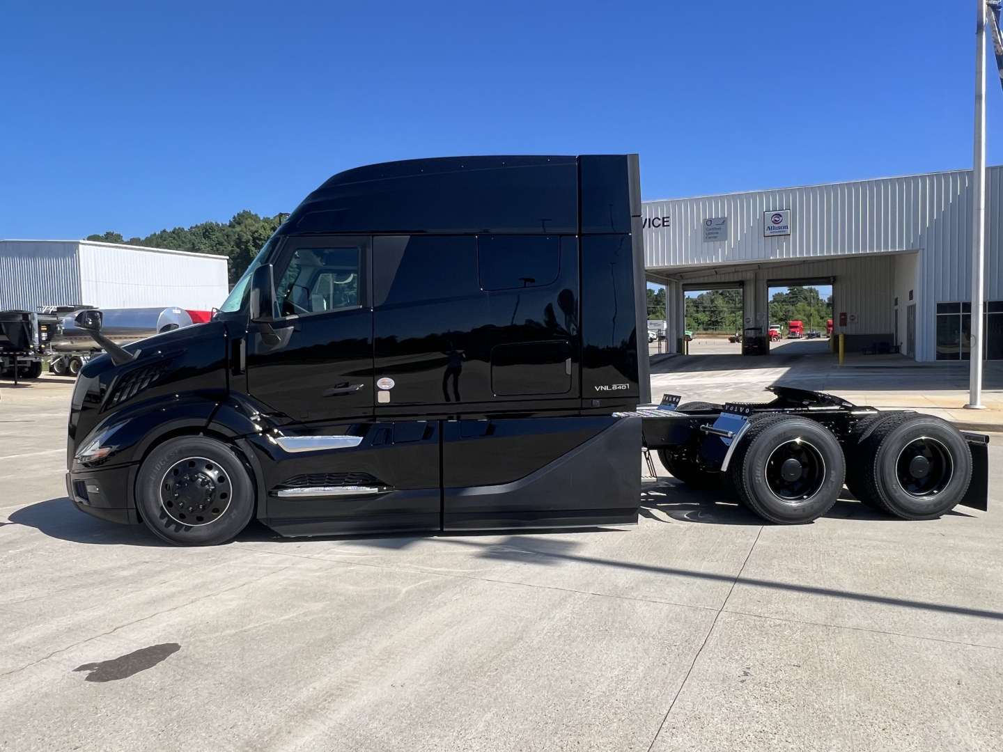 Semi truck in-service side view showing tractor with high-roof sleeper and dual rear axles, black paint, Volvo emblem on door.