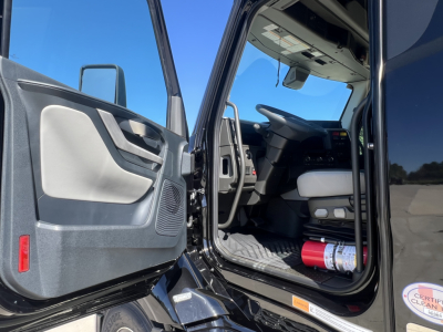 Interior of a Volvo VNL64T840 cab with open driver door showing steering wheel and seat, fire extinguisher on floor, and dashboard.