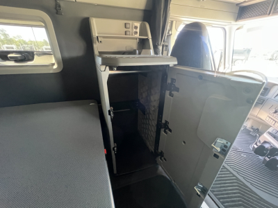 Volvo VNL64T840 interior cab area showing storage cabinet with open door and fold-down shelf, driver seat visible, dashboard and window frames in view.