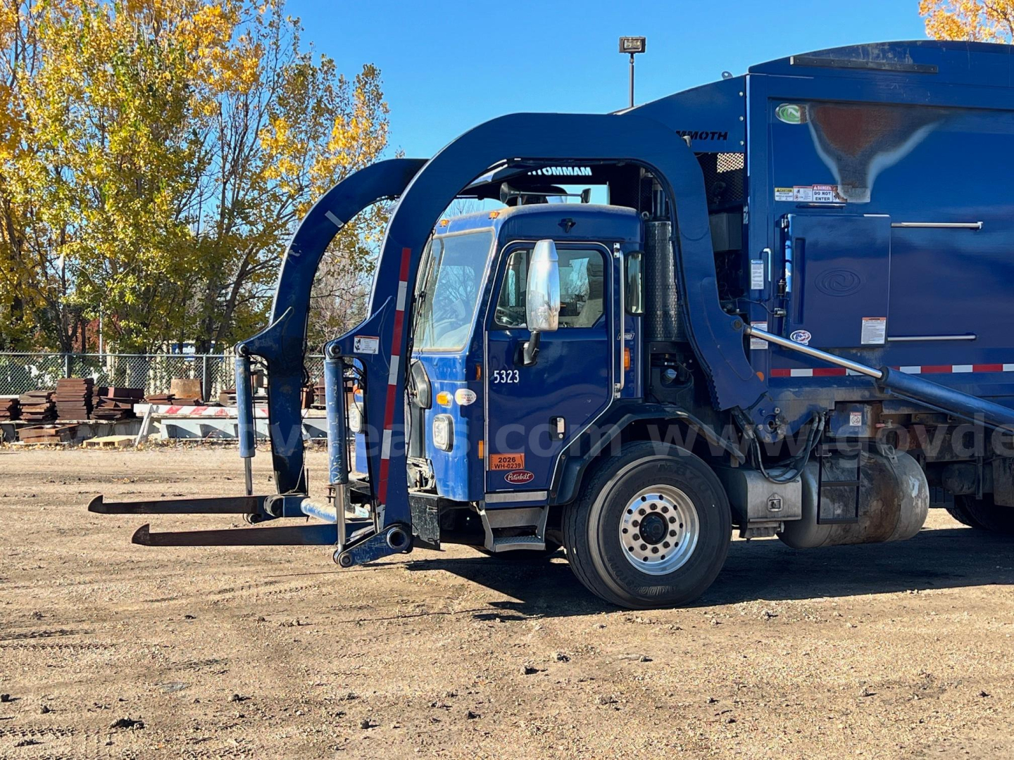Peterbilt 520 garbage truck in blue with rear compactor and articulated lift arms, side view of cab, VIN 3BPDLJ0X7MF110420 visible on image.