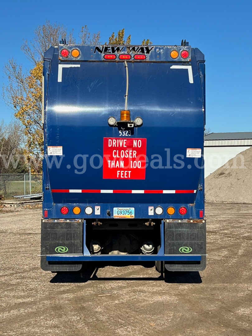 Rear view of a blue 2021 Peterbilt 520 garbage truck showing safety signage and rear lights