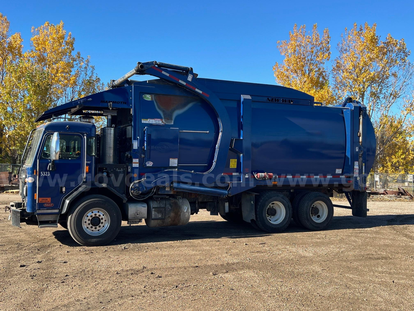 Garbage truck side view showing blue Peterbilt 520 with rear compactor and hydraulic arm.