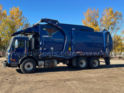 Garbage truck side view showing blue Peterbilt 520 with rear compactor and hydraulic arm.
