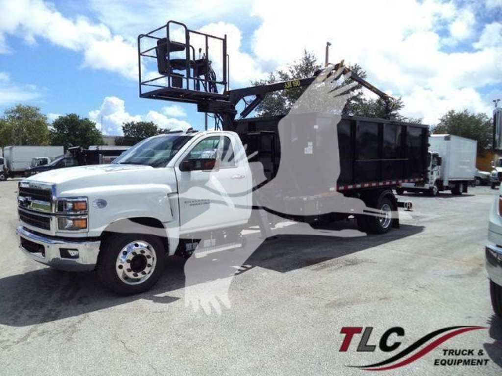 Chevrolet Silverado 6500HD roll-off truck with a black dump body, front cab white, mounted crane/basket on the side, in a dealership lot.