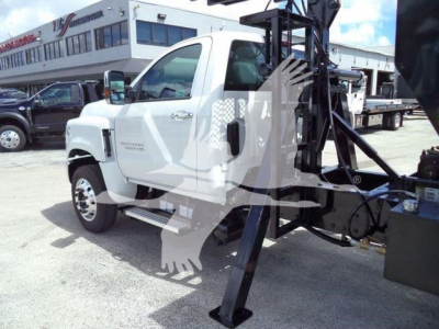 Chevrolet Silverado 6500HD roll-off truck with hydraulic lift and carrier, white cab, front side view, dealership lot in background.