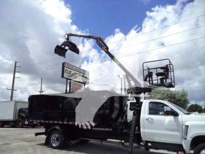 Truck bed with crane attachment on a white Chevrolet Silverado 6500HD chassis; overhead hydraulic grapple and worker platform in use.