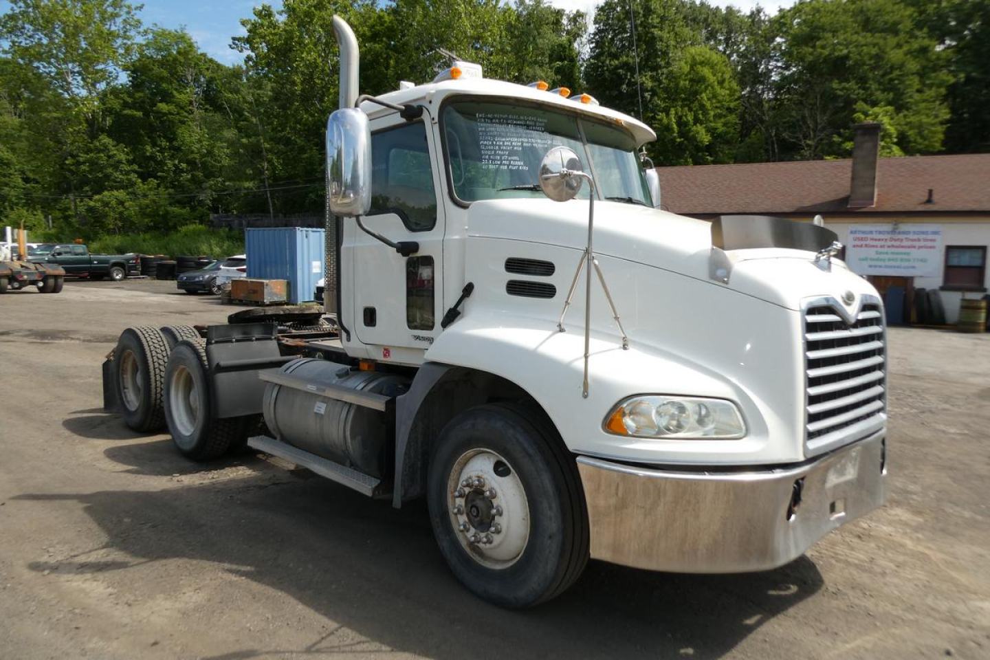 Truck cab in view showing front-left angle of a white 2007 Mack CXN613 Daycab with chrome bumper and grille, dual rear axles, and fuel tank.