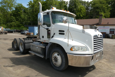 Truck cab in view showing front-left angle of a white 2007 Mack CXN613 Daycab with chrome bumper and grille, dual rear axles, and fuel tank.