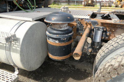 Air suspension/airbag shock reservoir near truck frame with cylindrical black tank and rusted clamps.