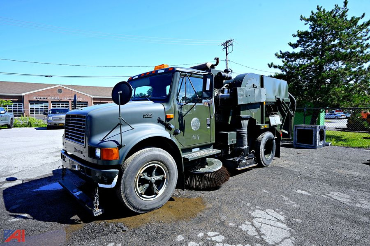 Iconic 1994 International 4600 sweeper truck in-service with large rear broom and vacuum housing, green cab, chrome grille, amber beacon on roof, front tires, side mirrors.