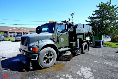 Iconic 1994 International 4600 sweeper truck in-service with large rear broom and vacuum housing, green cab, chrome grille, amber beacon on roof, front tires, side mirrors.