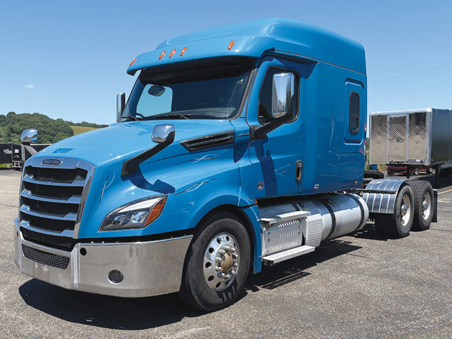 Truck engine bay view of a blue 2020 Freightliner Cascadia 126 conventional sleeper tractor showing front grille and side exhaust/cab details.