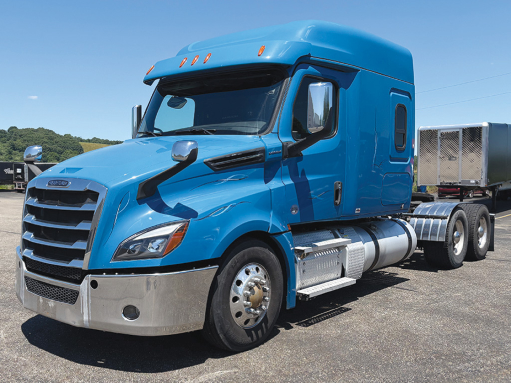 Truck engine bay view of a blue 2020 Freightliner Cascadia 126 conventional sleeper tractor showing front grille and side exhaust/cab details.