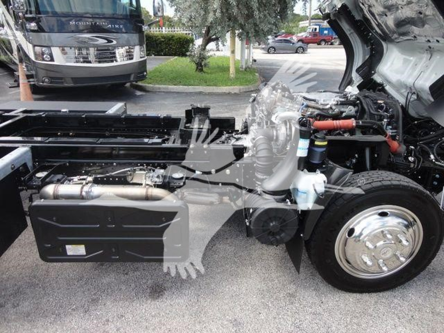 Engine bay of a 2023 Isuzu NPRR rollback truck showing side frame, exhaust, and front wheel with open hood revealing components; stock number NRRDSL22XLP visible in listing context.