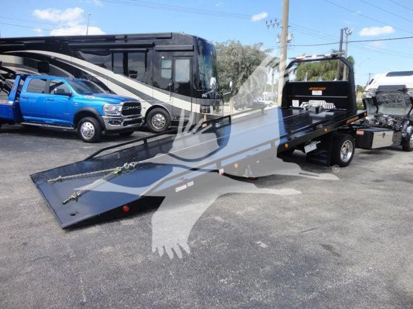 Isuzu NPR/Nrr rollback truck with a long flatbed car carrier in a parking lot, showcasing the ramp and companion vehicles in the background.
