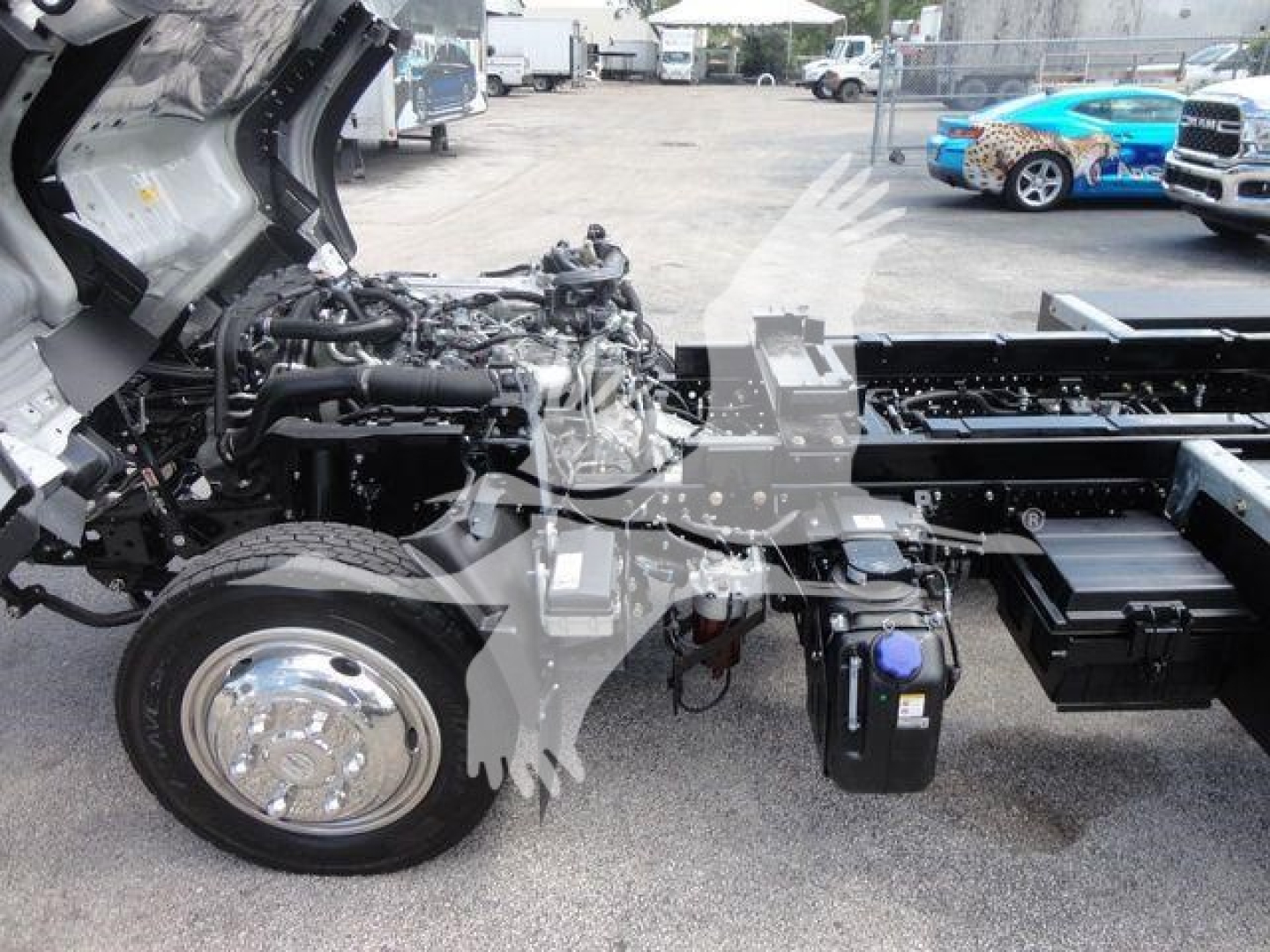 Isuzu NR series cab forward truck chassis showing engine bay and front suspension with wheel, diesel engine components, and hydraulic lines.