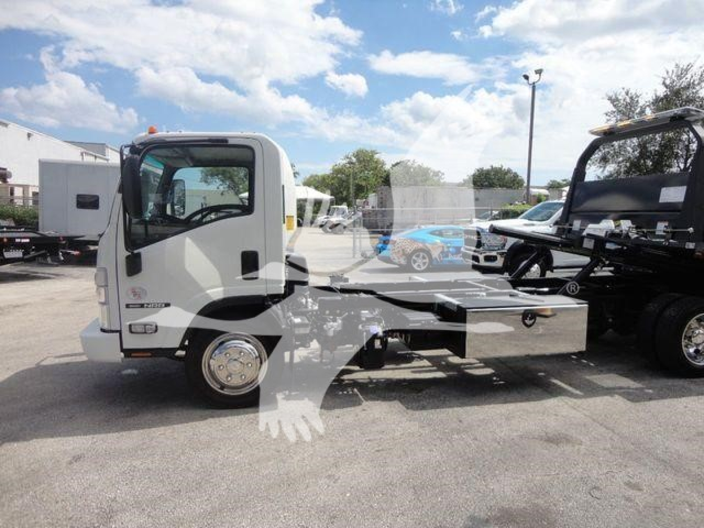 Isuzu NPR/Nrr roll-back truck chassis in a dealership lot, side view showing cab and frame, no bed installed.