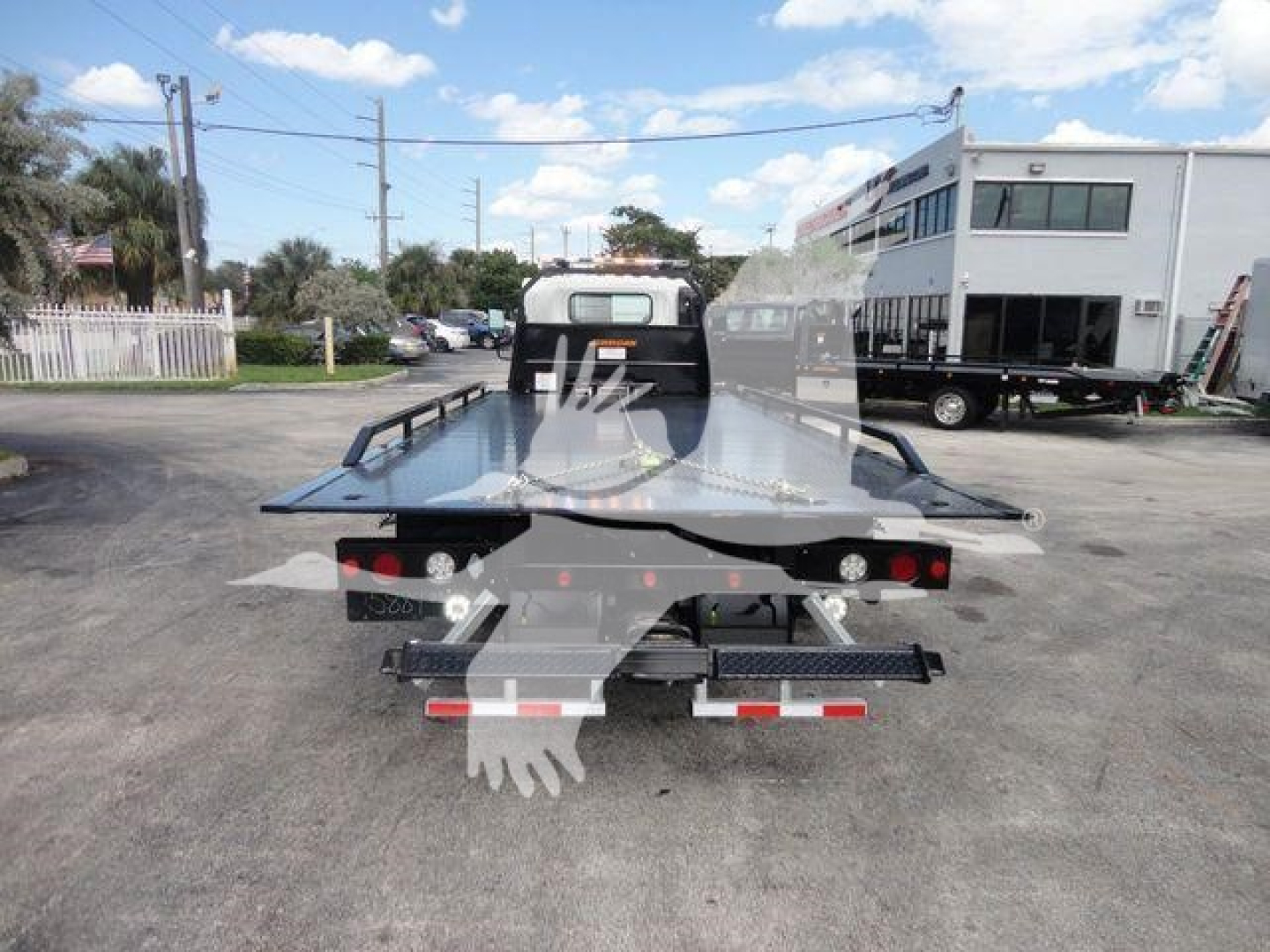Isuzu NPR/NRR rollback tow truck bed seen from rear, flatbed with ramps, rear lights, bumper, and towing equipment.