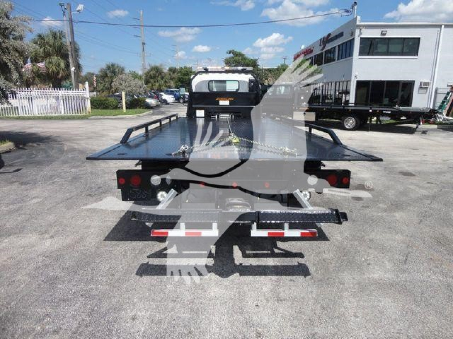 Isuzu NPRR rollback truck rear view showing flatbed with raised wheel lift and taillights.