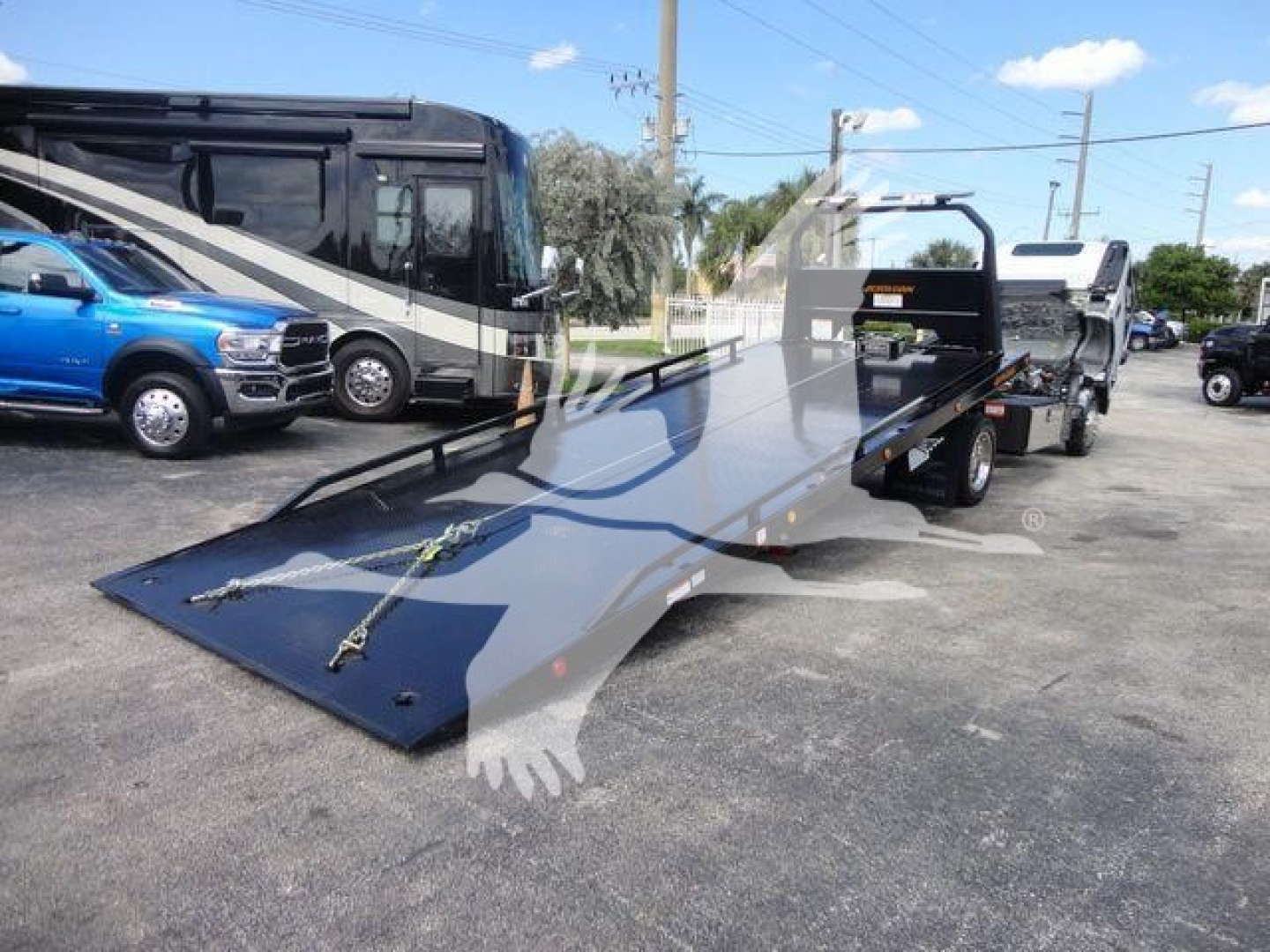 Isuzu NRR rollback truck with a tilted flatbed ramp and a blue pickup in the background