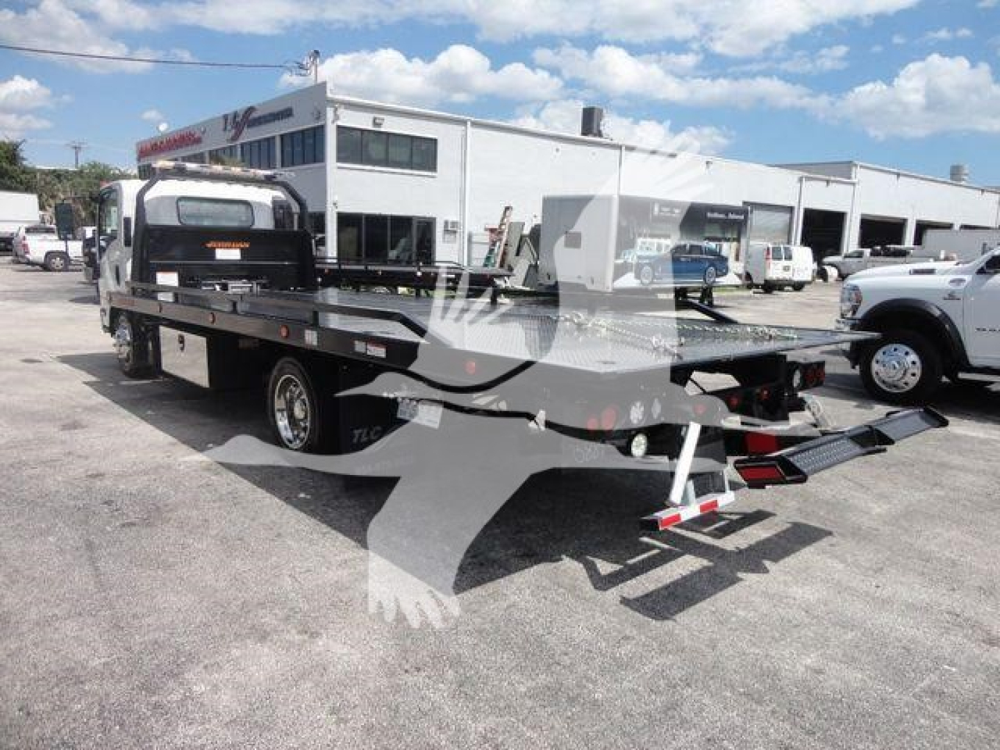 Isuzu NPRR rollback tow truck with flatbed and hydraulic ramps in a dealership lot