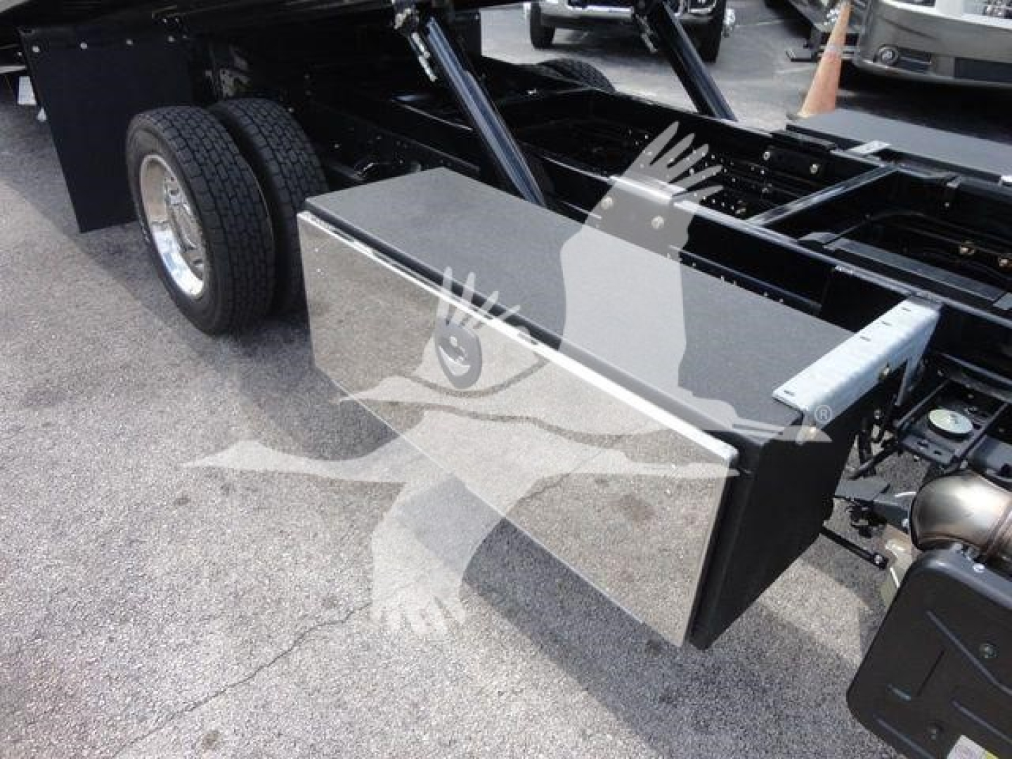 Isuzu NPR/NRR chassis side view showing a rectangular aluminum toolbox mounted near the cab with dual rear wheels and chassis framework in the background.