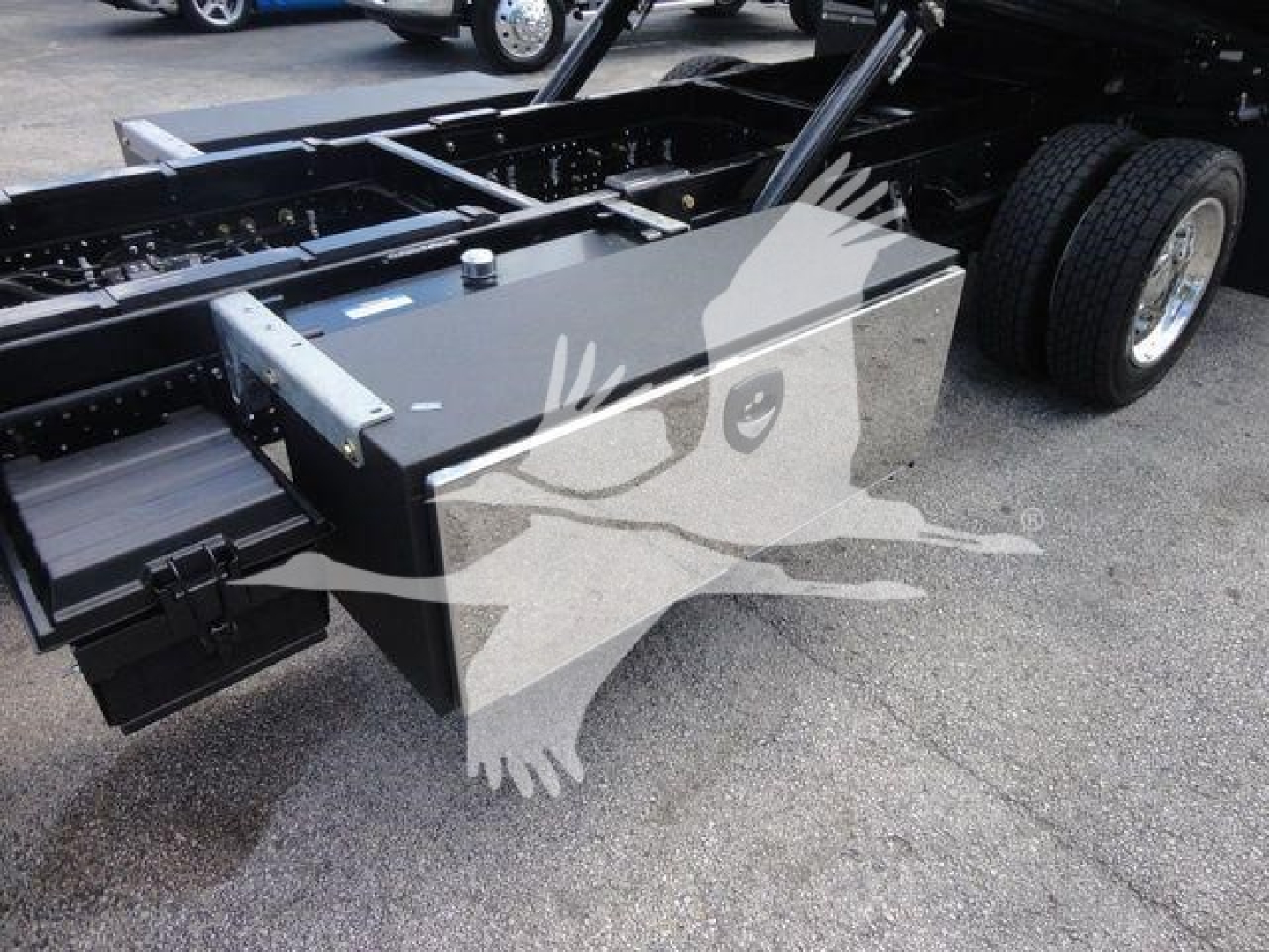 Truck chassis with a large rectangular toolbox mounted underframe showing metal toolbox and rear dual tires.
