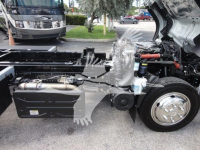 Engine bay of a 2023 Isuzu NPRR rollback truck showing side frame, exhaust, and front wheel with open hood revealing components; stock number NRRDSL22XLP visible in listing context.