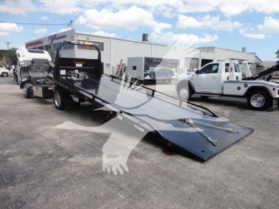 Truck rollback towbed with Isuzu NRR cab in background and a flatbed tilt surface visible in foreground.
