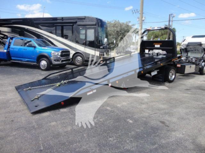 Isuzu NPR/Nrr rollback truck with a long flatbed car carrier in a parking lot, showcasing the ramp and companion vehicles in the background.