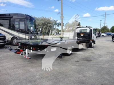 Isuzu NRR rollback tow truck with flatbed and rear ramps, white cab, parked lot with other vehicles.