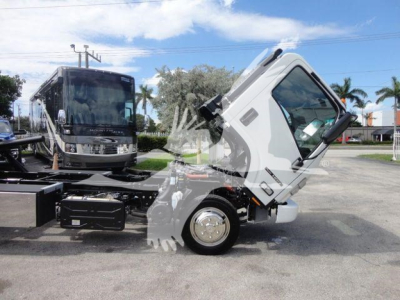 Isuzu NPR/NQR series roll-back truck cab tilted forward showing front axle and wheel; background shows another vehicle and dealership lot.