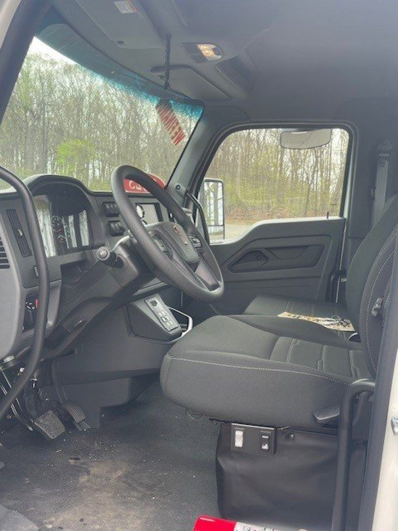 Interior of a Kenworth T280 cab showing driver seat, steering wheel, dashboard, and entry area; visible windshield and side window with outdoor trees.