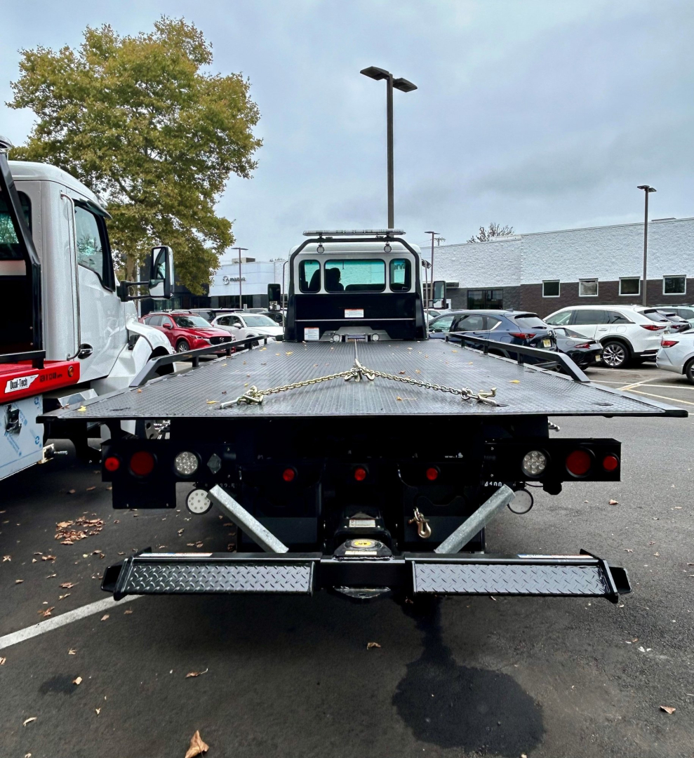 Kenworth T280 tow truck flatbed rear view showing hydraulic equipment, taillights, and ramp with securing chains.
