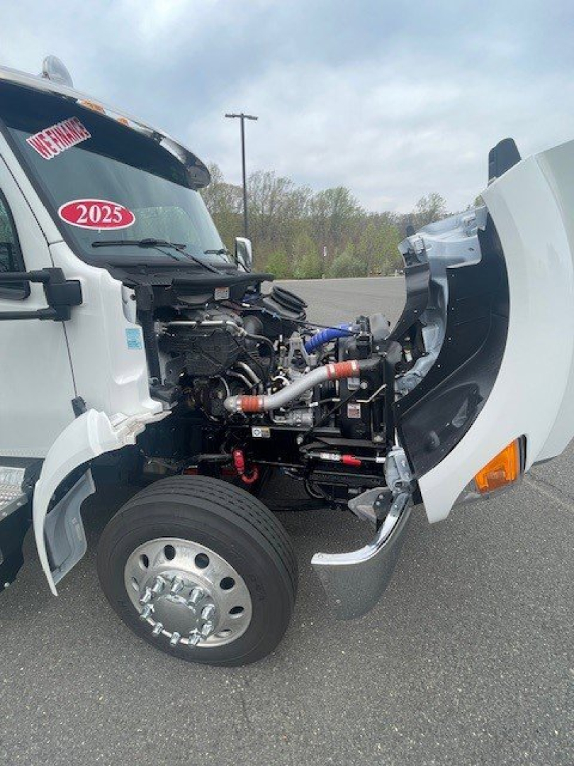 Kenworth T280 front engine bay with exposed diesel engine and intake components, white cab, 2025 badge on windshield, open hood showing hoses and metal piping.