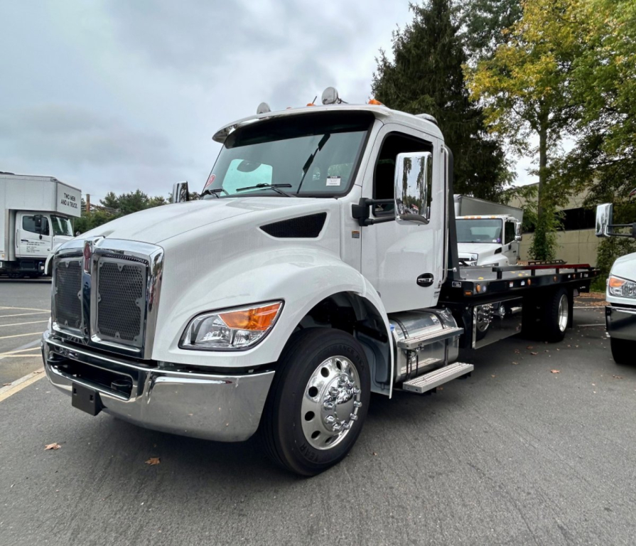 Kenworth T280 tow truck side view showing front chrome grille, hood, dual rear wheels, and flatbed in a dealership lot.