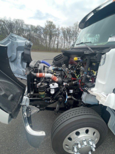 Kenworth T280 engine bay showing exposed engine components, hoses, wiring, and front wheel with hubcap.