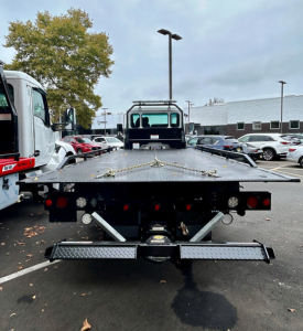 Kenworth T280 tow truck flatbed rear view showing hydraulic equipment, taillights, and ramp with securing chains.
